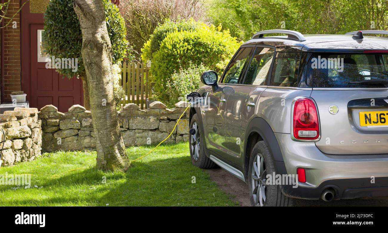 BUCKINGHAMSHIRE, UK - April 09, 2022. Electric car charging at home. Electric Mini Countryman parked outside a house, plugged in and recharging. Stock Photo