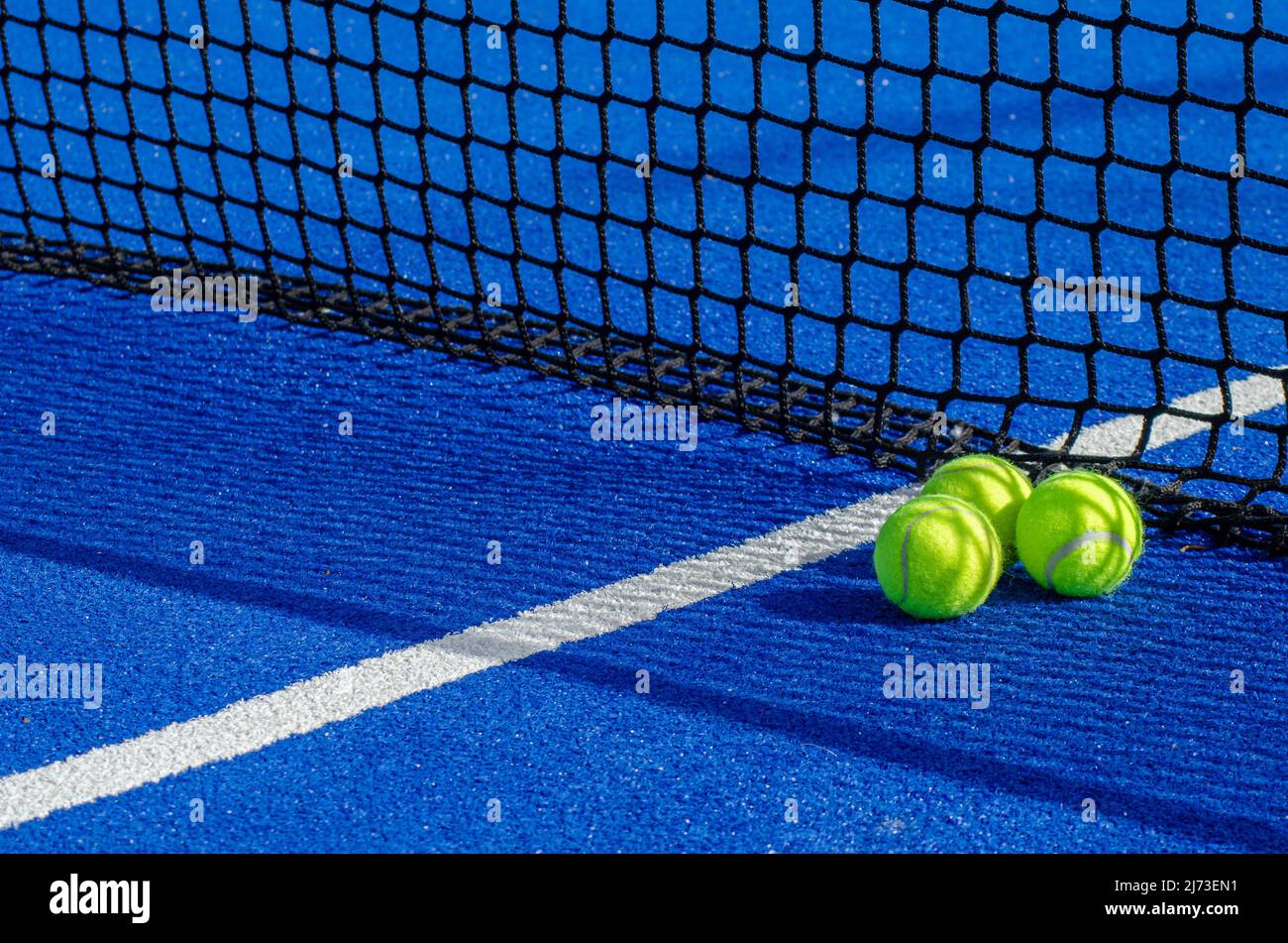 blue paddle tennis court, three balls near the net and the center line