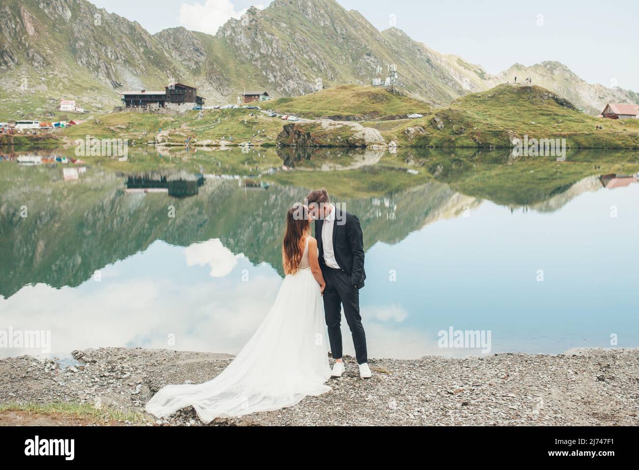 Romantic wedding couple in love standing on backdrop of a lake and mountain landscape. Happy marriage couple. Loving man and woman at marriage day. Stock Photo