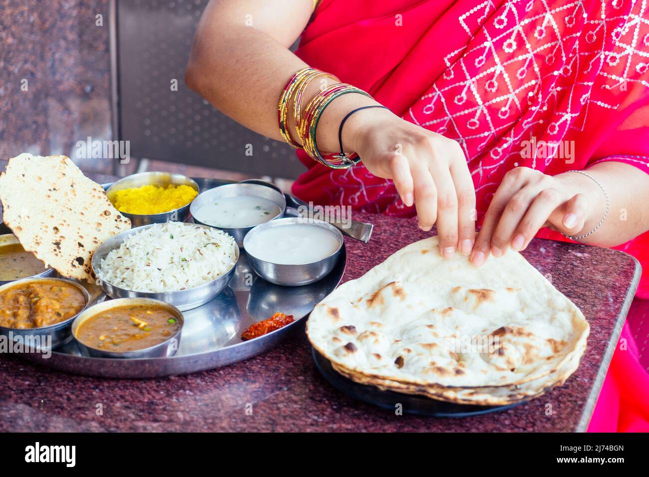 close up photo of Indian traditional vegetarian thali from rice, dal, potatoes, tomato salad on metal plate ,female hands roti india tortilla Chapati Stock Photo