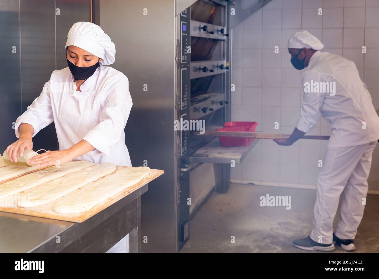 Latina sprinkling raw cocas with oil before baking in bakery Stock Photo