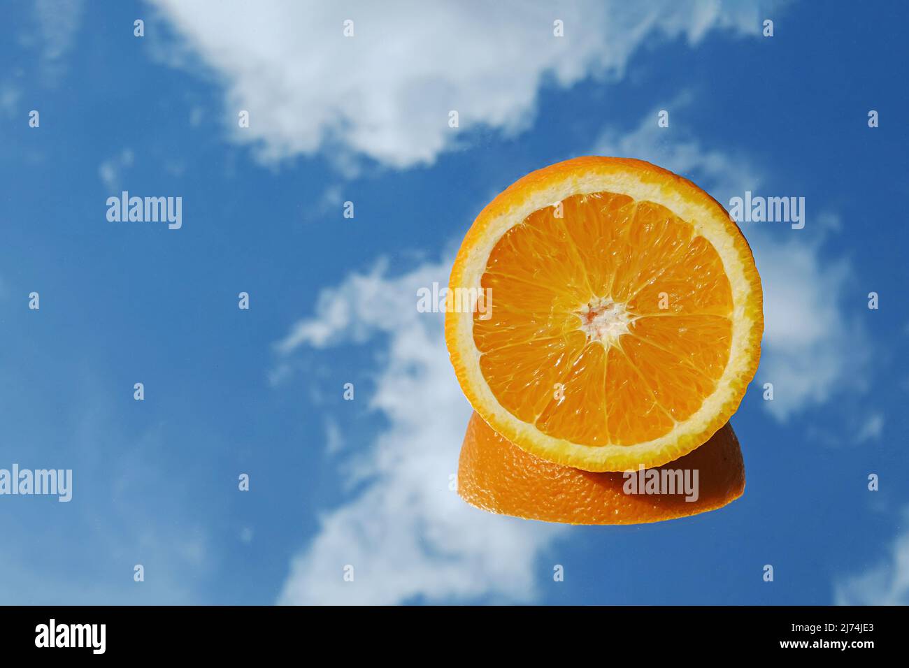 Orange citrus fruit tropical orange on blue sky and clouds background. Orange in the mirror surreal minimal concept. Stock Photo