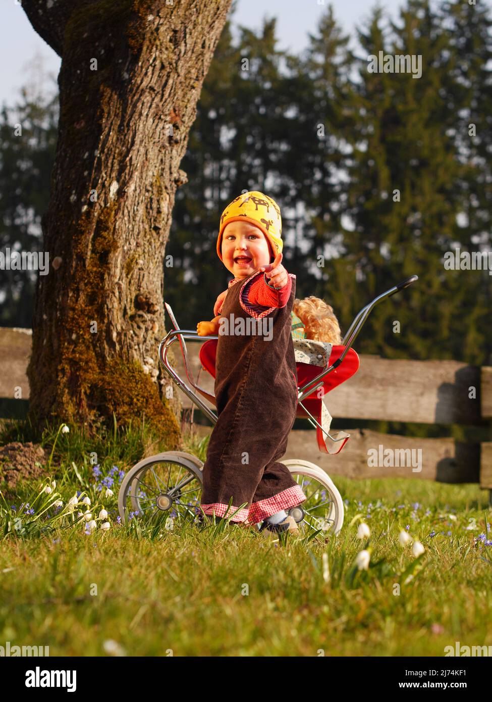 Kind spielt mit Puppenwagen und zeigt auf  Kamera Stock Photo