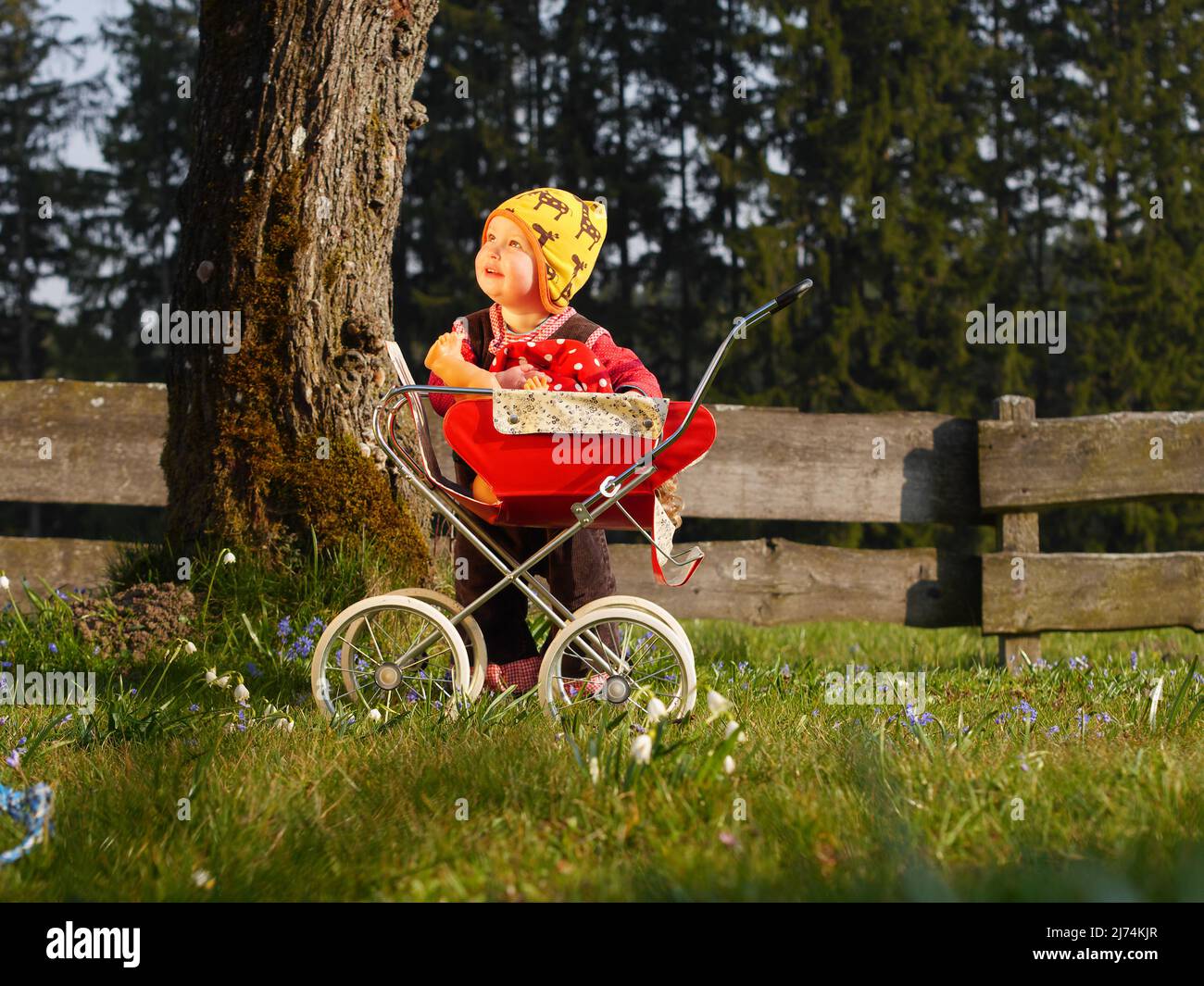 Kind spielt mit Puppenwagen im Garten und schaut zum Himmel Stock Photo
