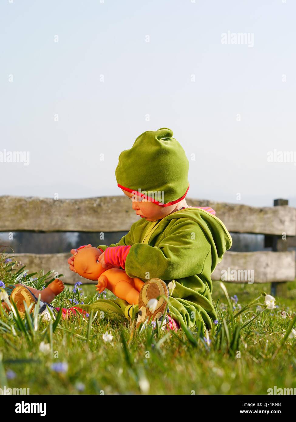 Mädchen sitzt im Gras und spielt mit Puppe Stock Photo