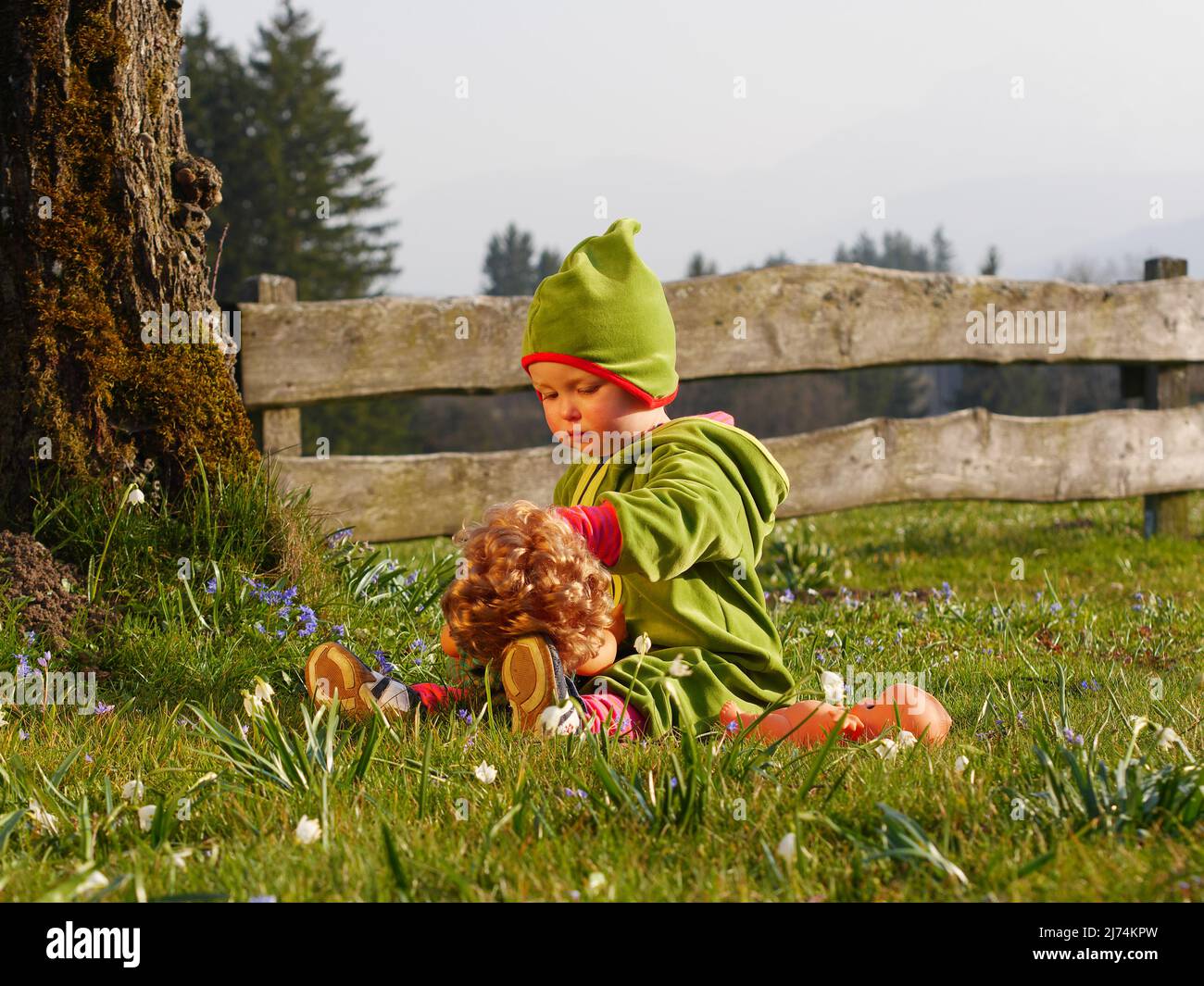 Mädchen sitzt im Garten und spielt mit Puppe Stock Photo