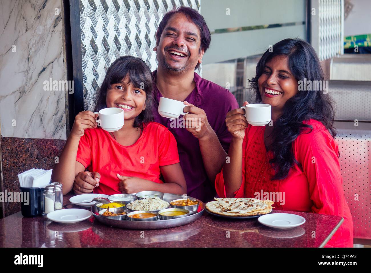 beautiful mother and happy father eating thali with daughter in cafe and drinking masala chai Stock Photo