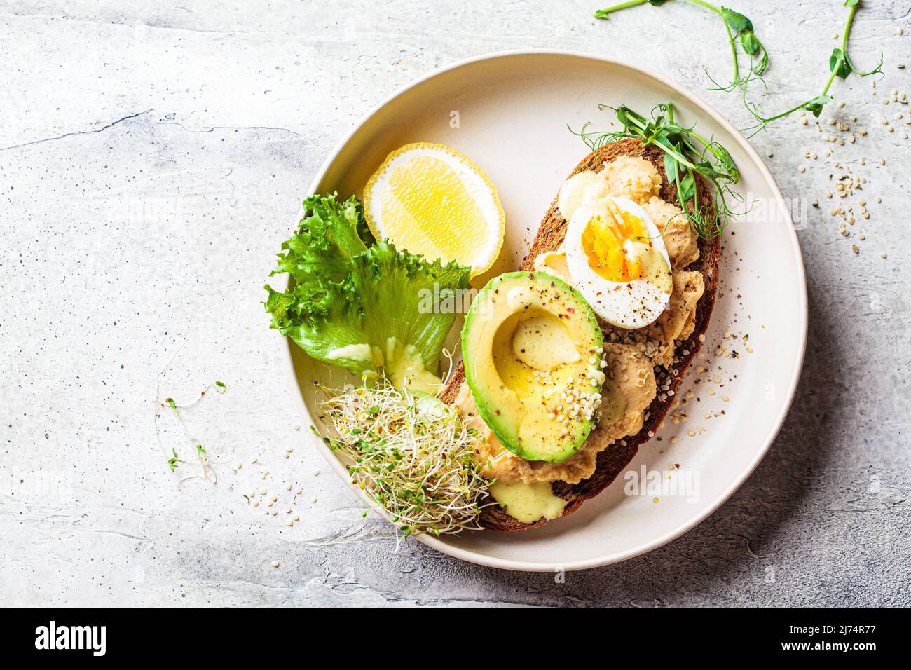 Balanced breakfast toast with pate, avocado, egg and sprouts on a white plate, top view, copy space. Stock Photo