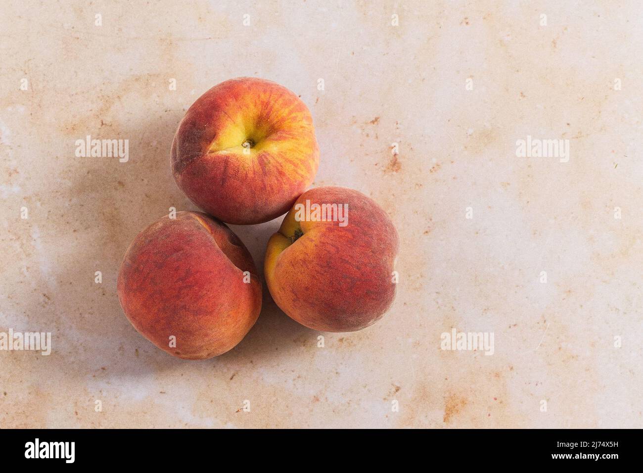 Three peaches on a pink marble backdrop. Stock Photo