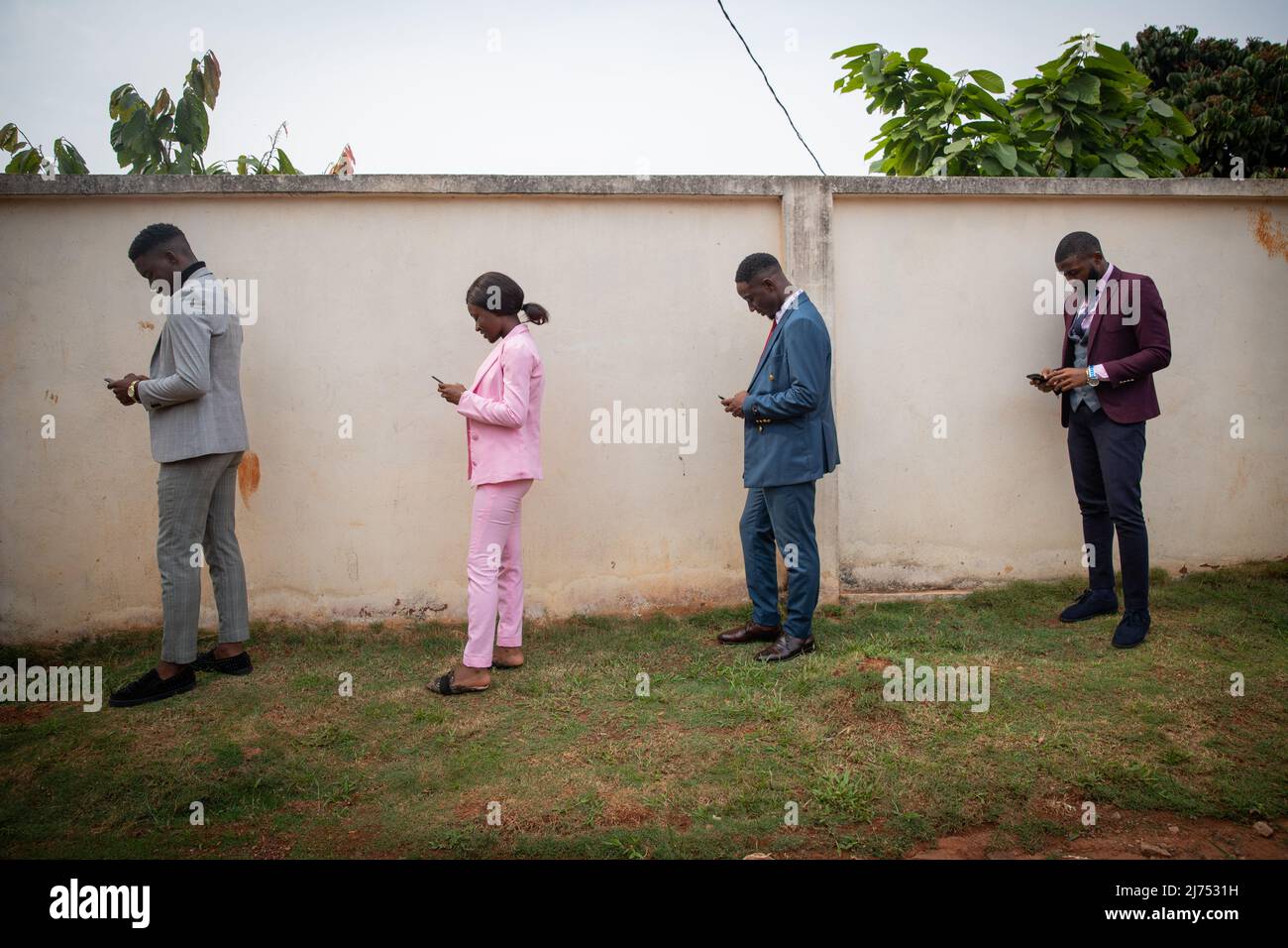 A group of well-dressed young Africans use their smartphones in line while keeping a safe distance during the pandemic Stock Photo