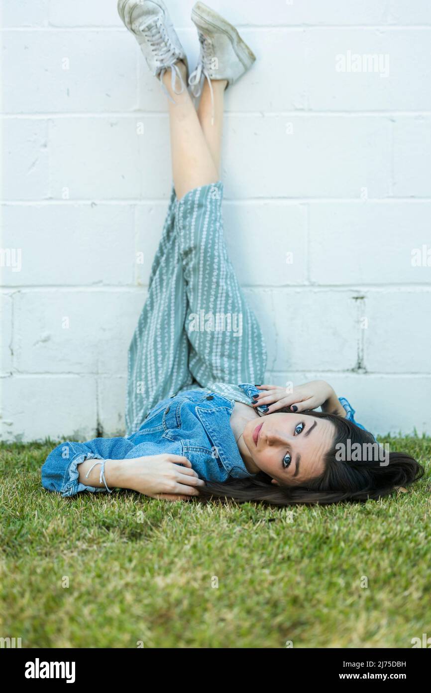 A teenage girl lying on the ground with her legs propped up on a wall with a serious look for a cool angle with copy space for text Stock Photo