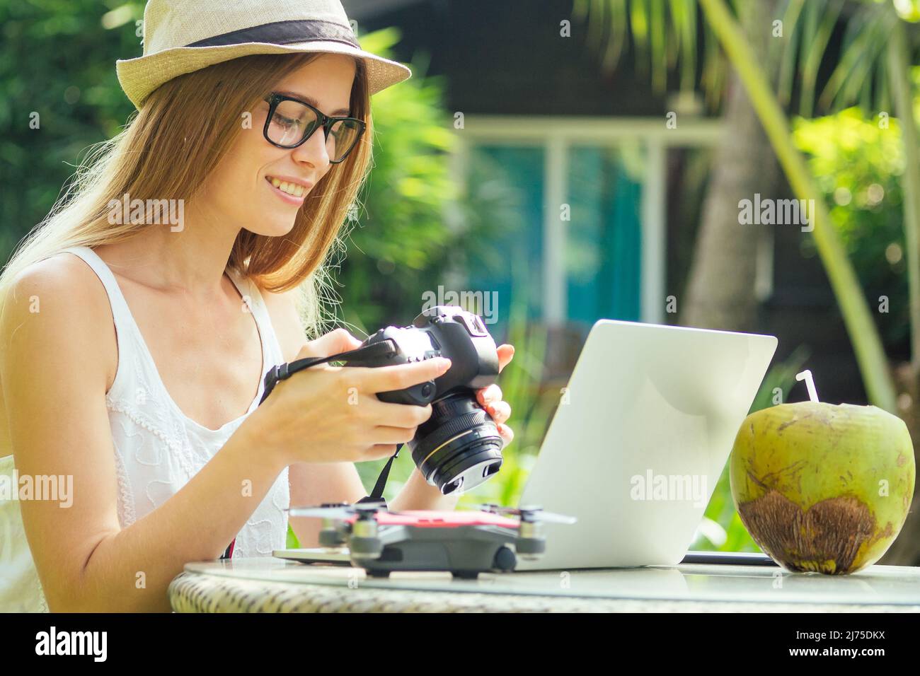 Female photographer inserting or removing a memory card in her professional dslr camera as she sits at a desk with her laptop at paradise beach green Stock Photo