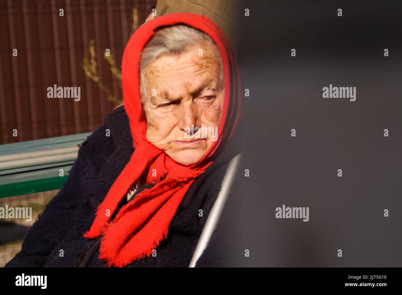 Defocus ukrainian elderly woman in red shawl with crutches sitting outside. Woman 90 years old. Alone person. Closeup portrait. Sick and homecare Stock Photo
