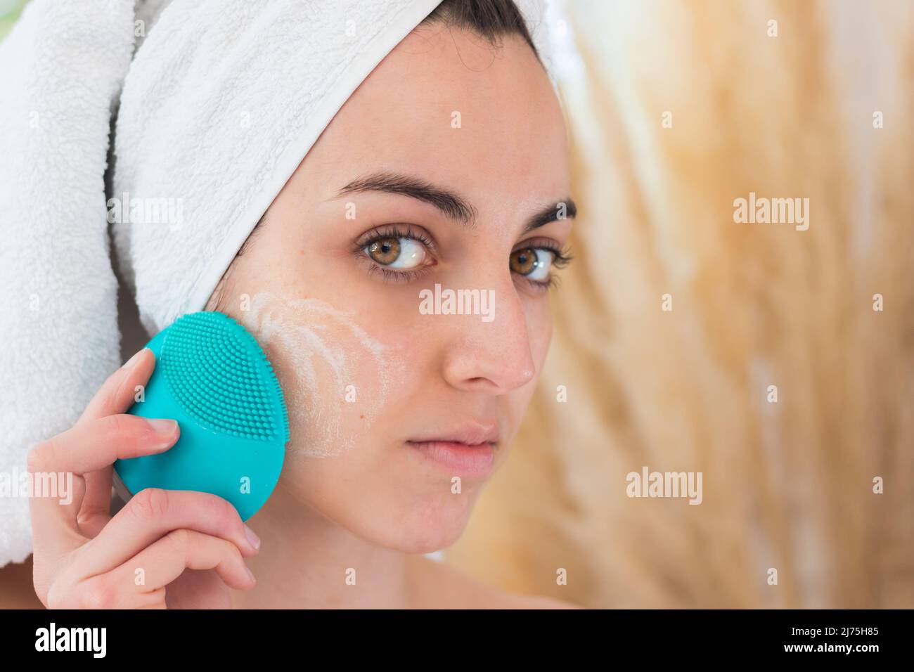 Close up portrait of young woman washing her face with a silicone brush for cleansing pores. Cosmetic products Stock Photo