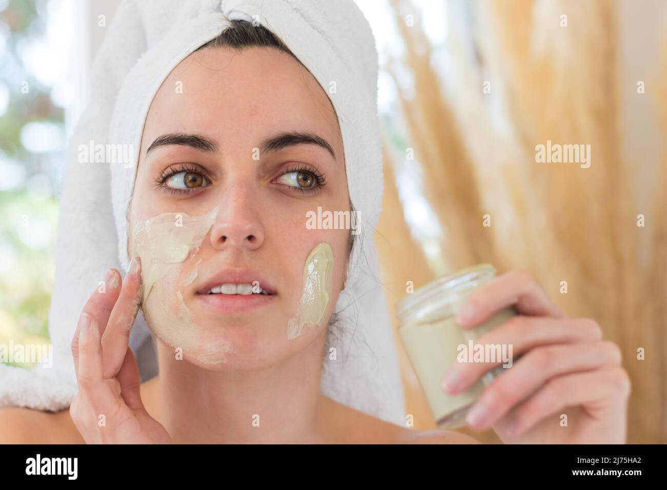 Portrait of beautiful woman putting cosmetic mask on her face to purify and refresh skin as home