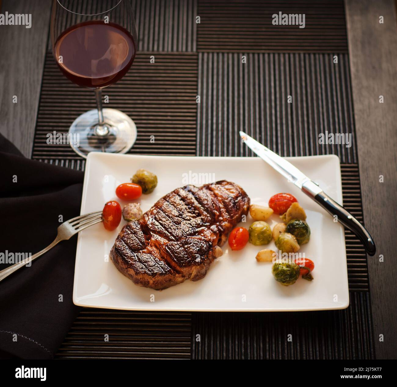 Whole Steak on a white plate with Roasted Vegetables and a Glass of Red Wine Stock Photo