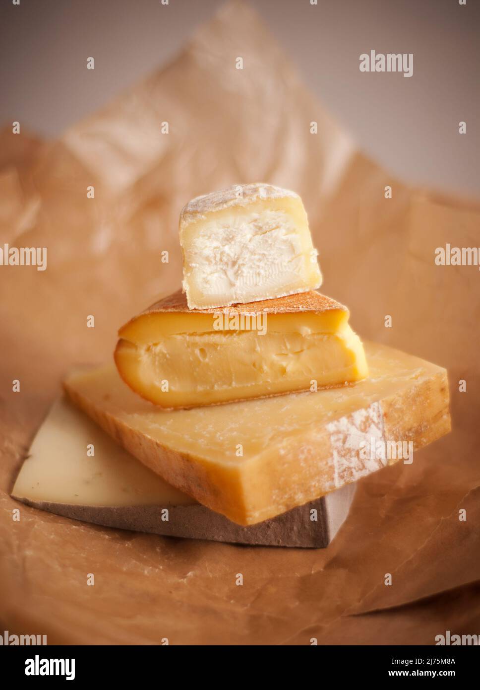 Stack of assorted gourmet cheeses on parchment paper Stock Photo