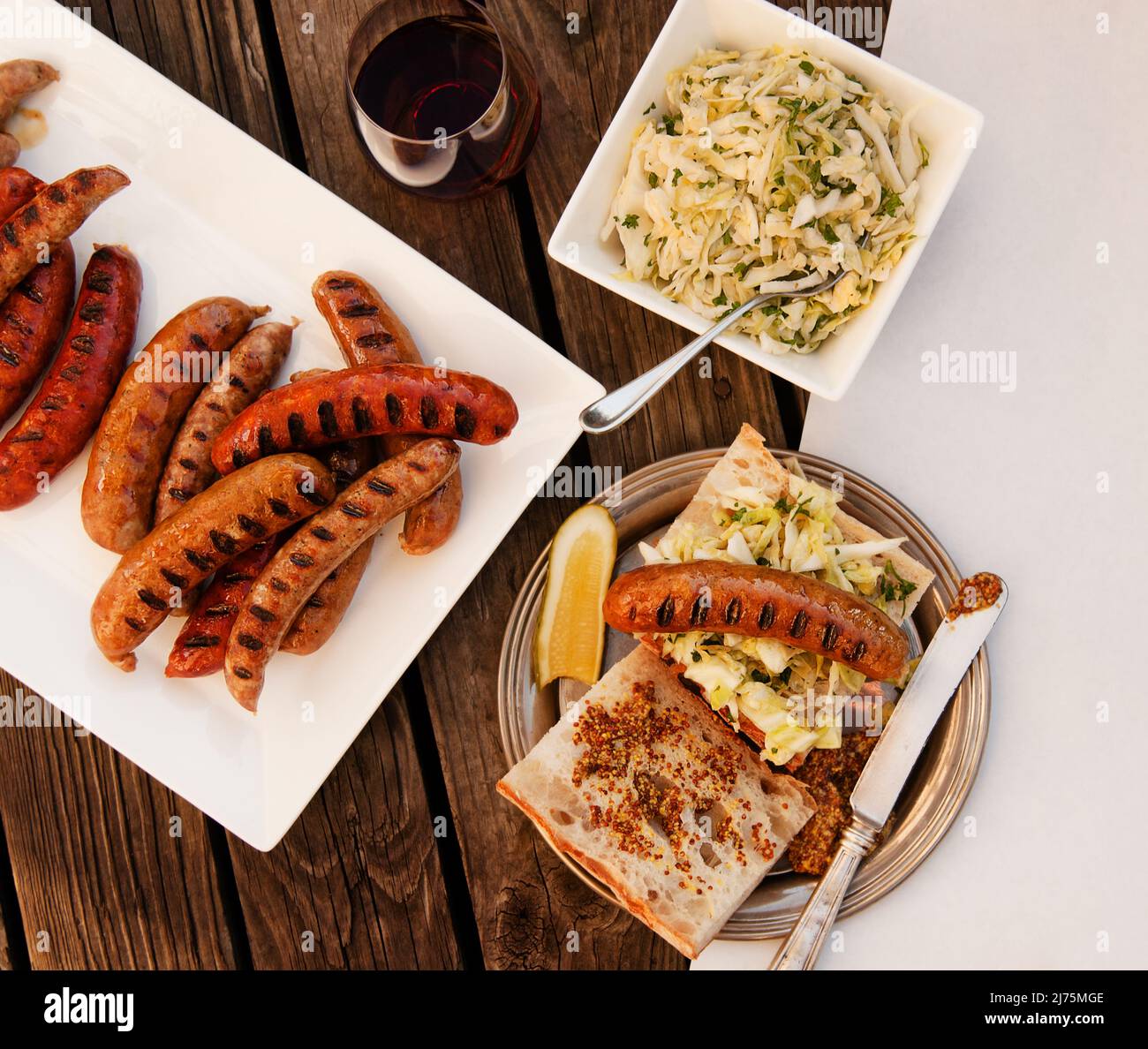 Grilled Sausage Sandwich with Cole Slaw, Pickles, Mustard and a Platter of Grilled Sausage; From Above Stock Photo