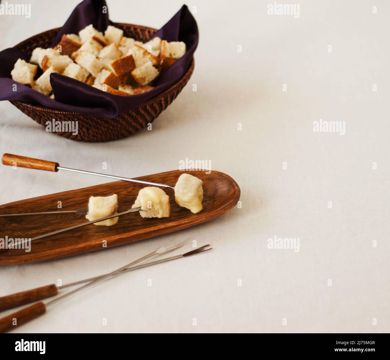 Three Pieces of Cheese Fondue Dipped Bread on Forks; Bowl of Bread Cubes in Background Stock Photo