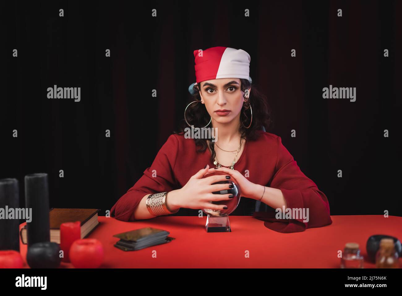 Gypsy fortune teller touching magic orb near tarot and candles isolated