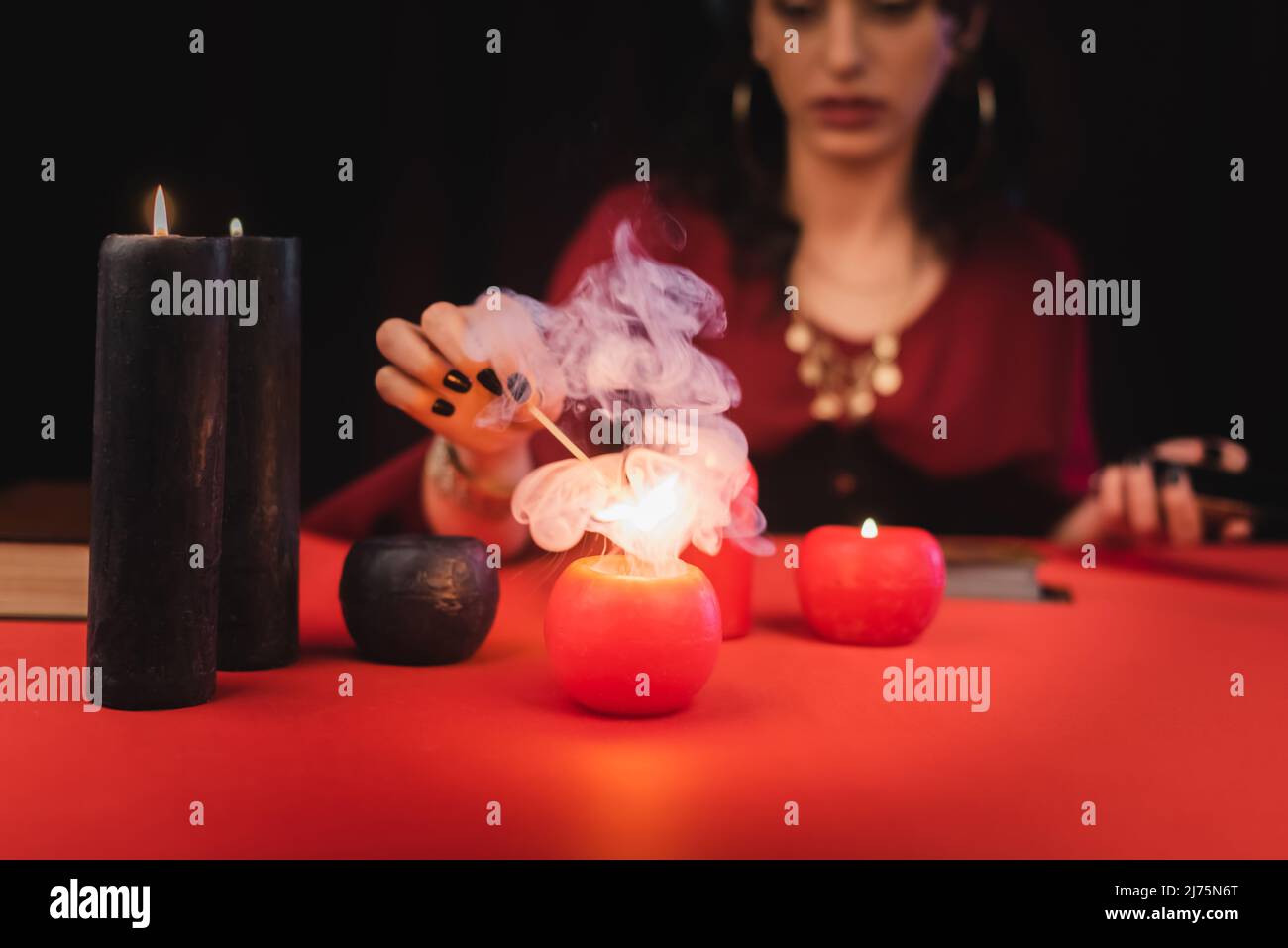 Cropped view of blurred soothsayer burning red candle on table isolated on black Stock Photo