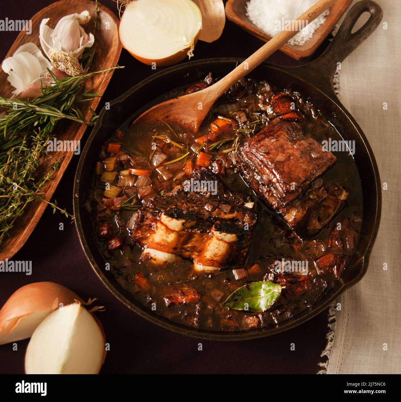 Beef Braising in Cast iron pan with herbs and vegetables Stock Photo