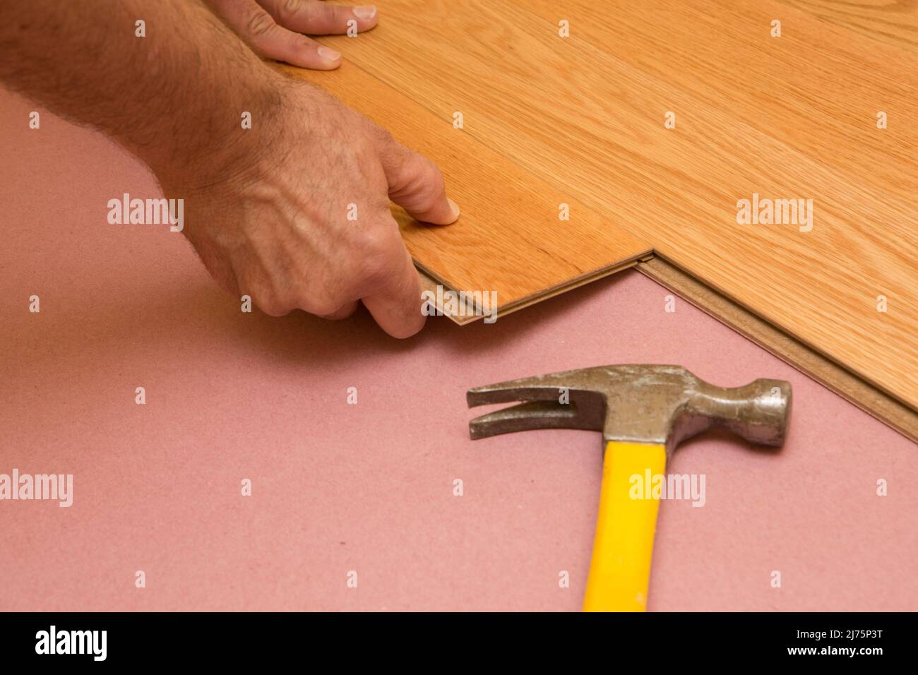 Series of shots of engineered hardwood floor being installed by a worker over pink felt paper using hand tools Stock Photo