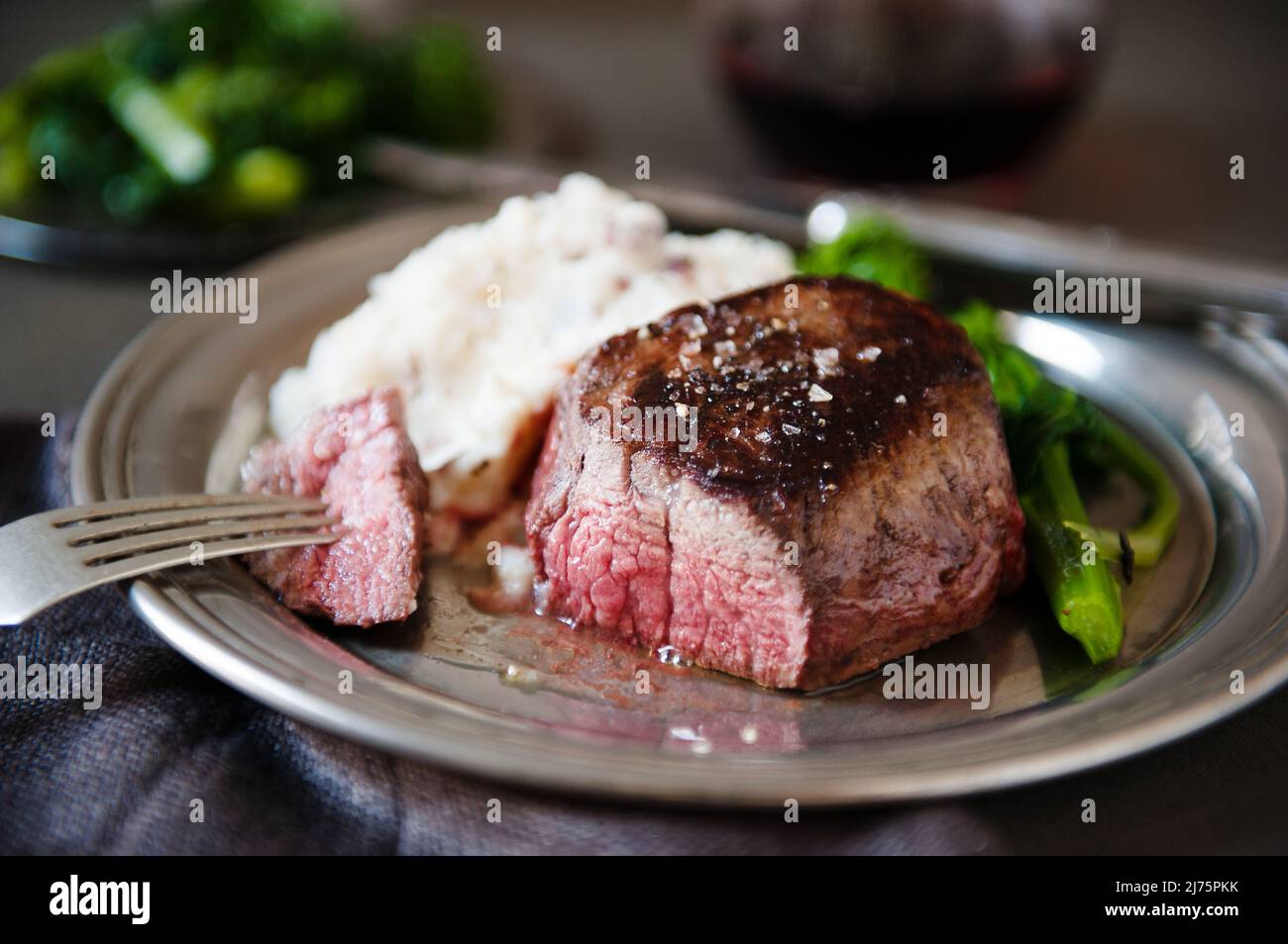 Filet Mignon with a Piece Pierced on a Fork; Served with Mashed Potatoes and Broccoli Rabe Stock Photo
