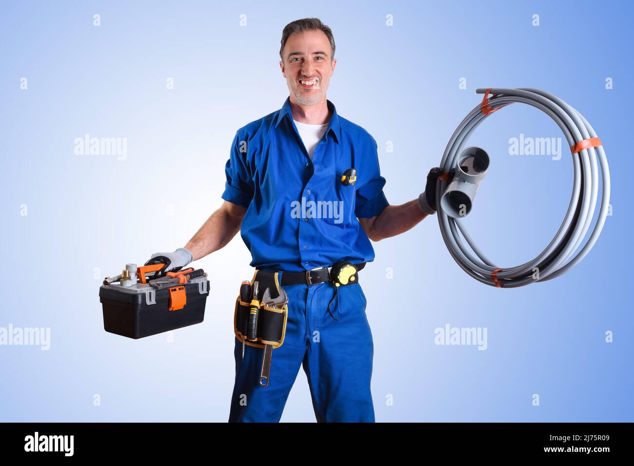 Portrait of uniformed plumber with work tools in hands and blue gradient isolated background. Front view. Horizontal composition. Stock Photo