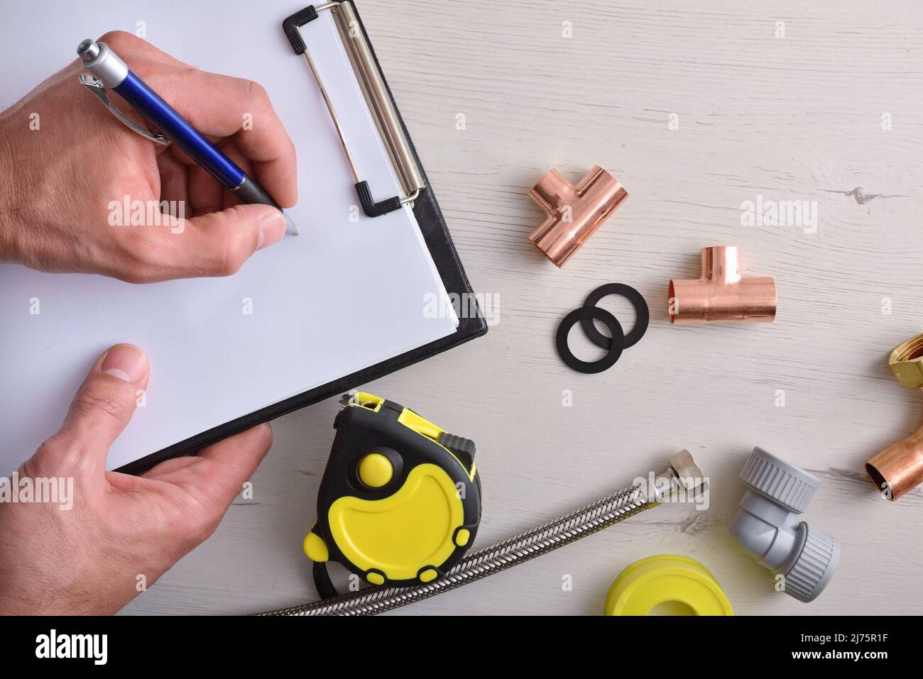 Review and preparation of plumbing material for a job with hands pointing on a notepad and plumbing material on a wooden table. Top view. Horizontal c Stock Photo
