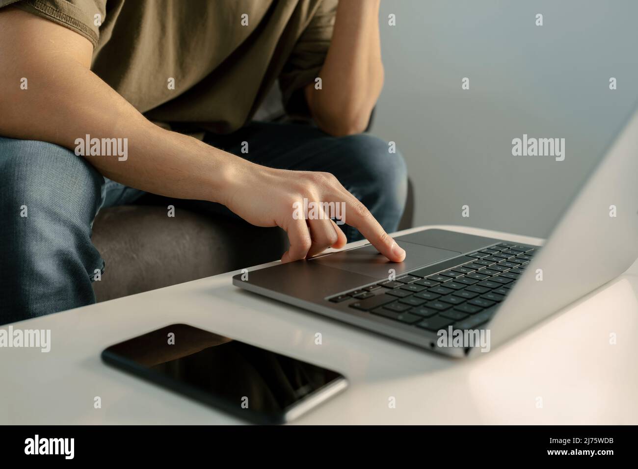 Computer, adult male touching touchpad of laptop lying on table, living room and remote workspace, his phone is on the table and the young man is chec Stock Photo
