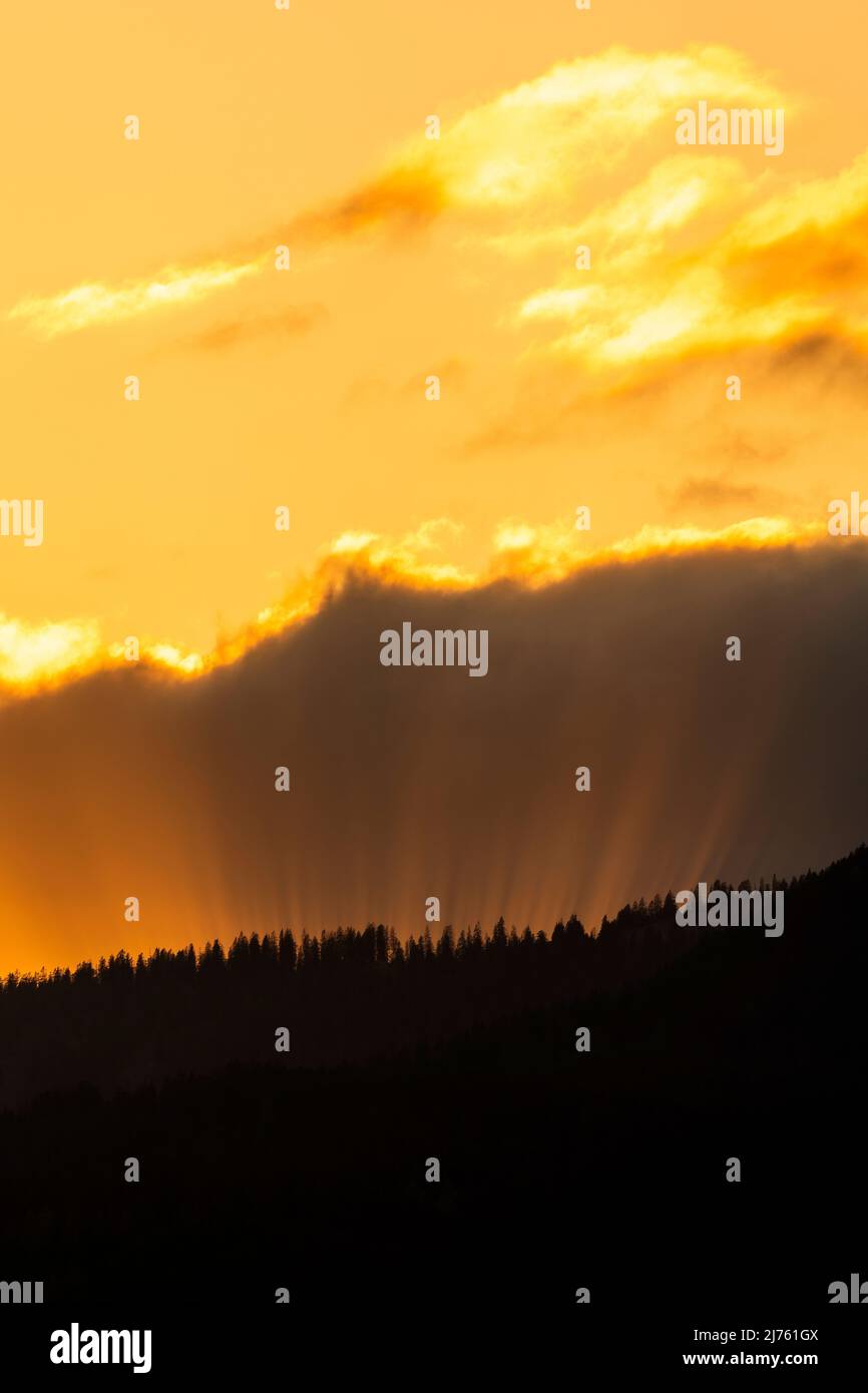 Sun rays in the evening red, break through between cloud and forested mountain. Stock Photo
