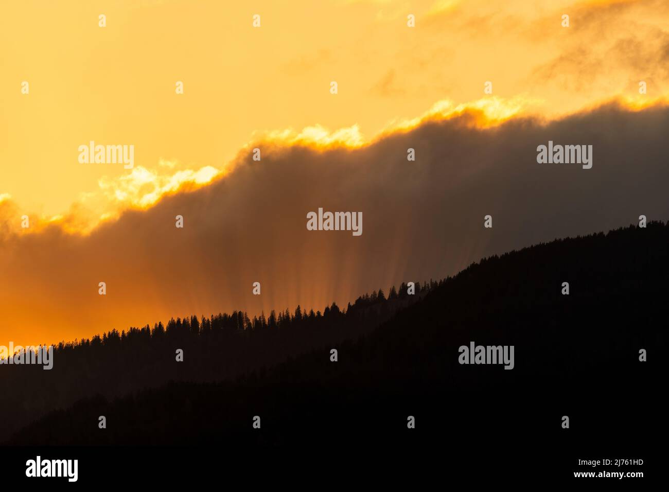 Sun rays in the evening red, break through between cloud and forested mountain. Stock Photo