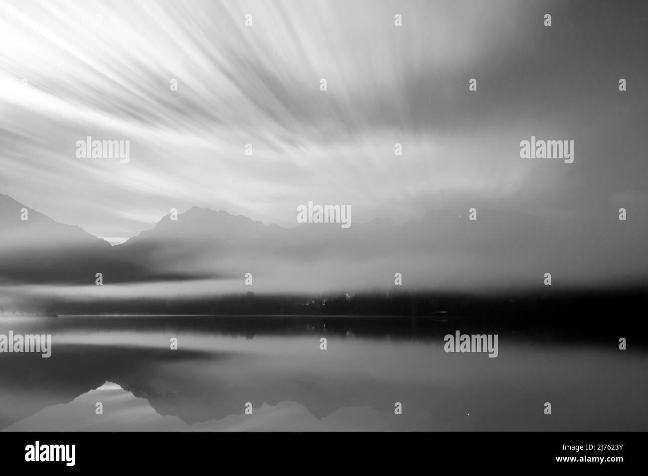 Night shot with clouds and fog at the Barmsee near Krün in the Bavarian Alps with a view of the Karwendel, the mountain station of the Karwendelbahn is just shining through the fog wall. Black and white shot. Stock Photo