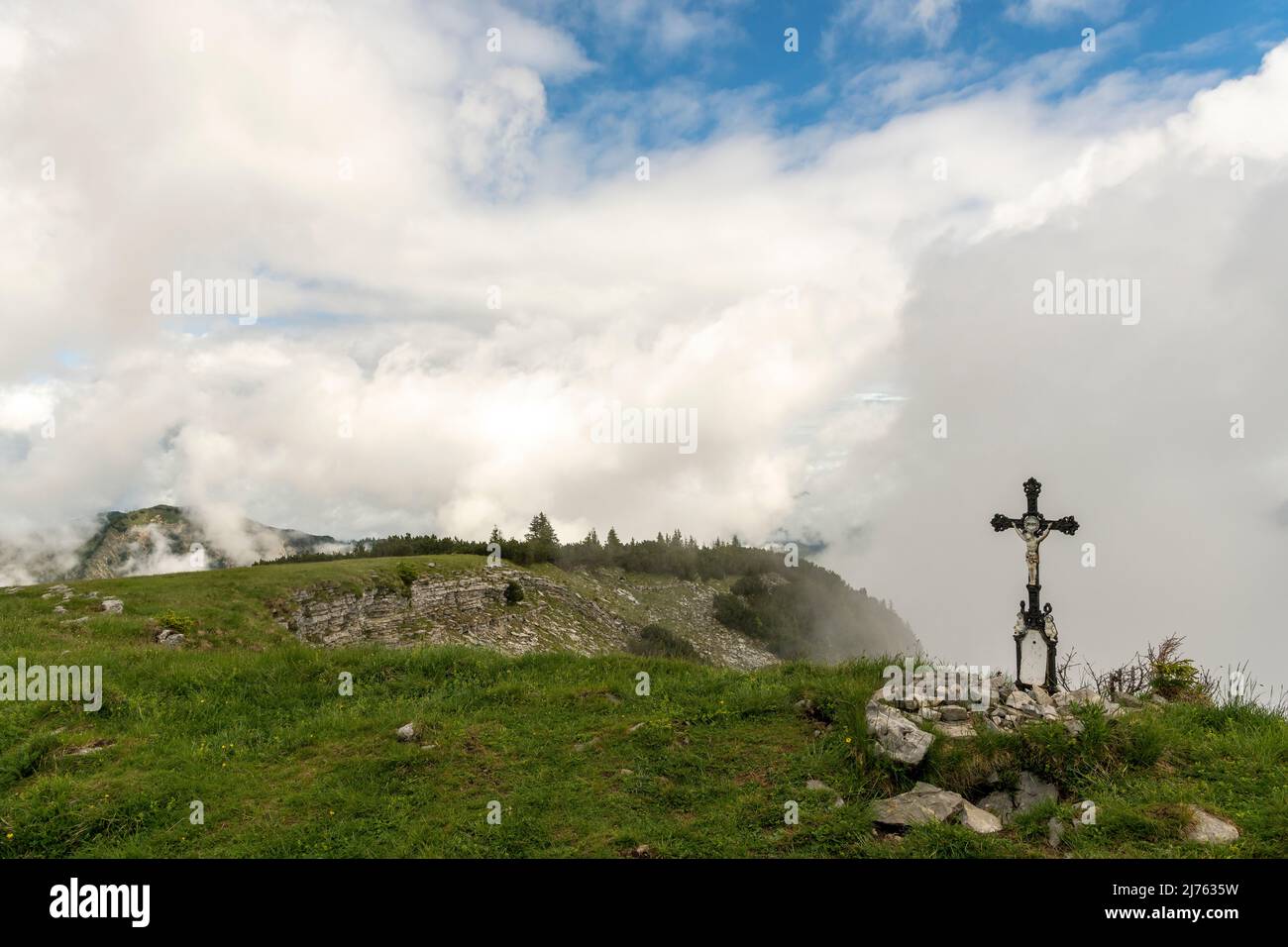 The small metal summit cross on the Vorderskopf in the Karwendel, in the background dense clouds and some blue sky. Stock Photo