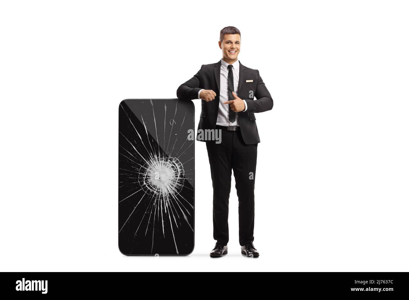 Man in a black suit and tie leaning on a big smartphone with a broken screen and pointing isolated on white background Stock Photo