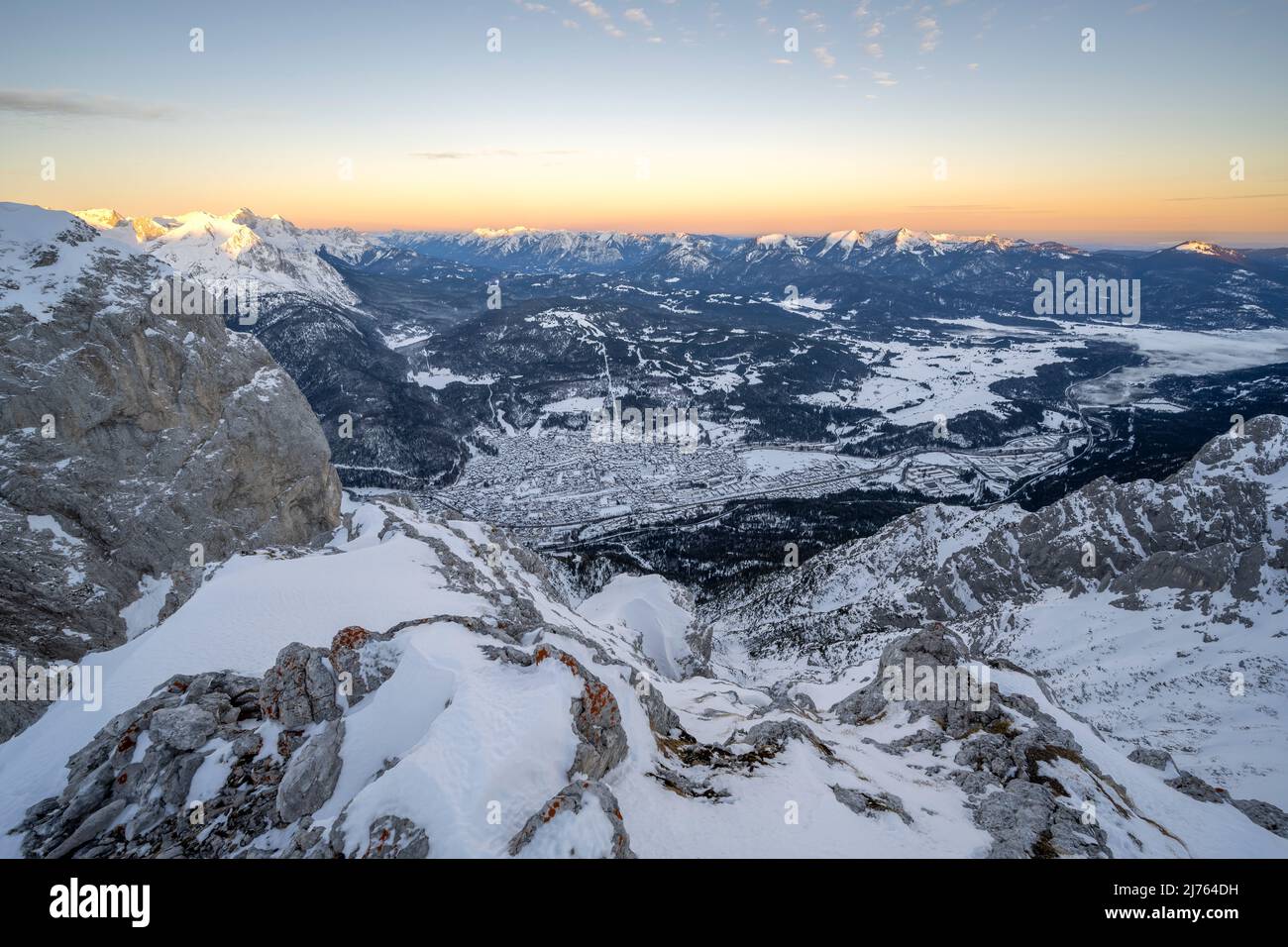 View from the western Karwendel, over rocks and snow ind he Werdenfelser Land in winter, with the market town Mittenwald, the Kranzberg, the Bavarian Prealps and towards Garmisch-Partenkirchen, with the Zugspitze in the background, while soft colors of dawn are in the sky. Stock Photo
