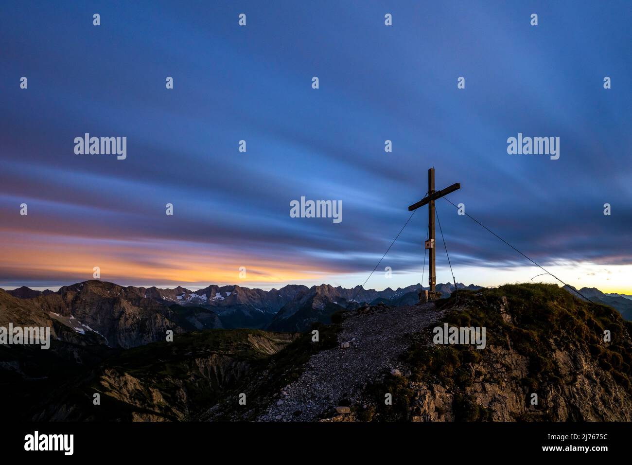The summit cross of the Mondscheinspitze in the Karwendel, shortly after sunset. Through the long exposure, the colors of the night show and the clouds blur. Stock Photo