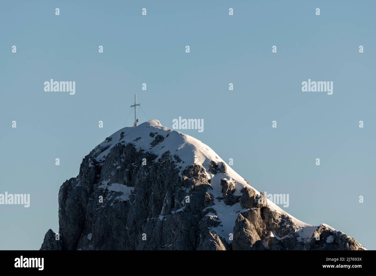 The snowed-in summit cross of the Westliche Karwendelspitze in the Karwendel above Mittenwald, near the mountain station of the Karwendelbahn. The cross is partially iced, in the background the blue sky. Stock Photo