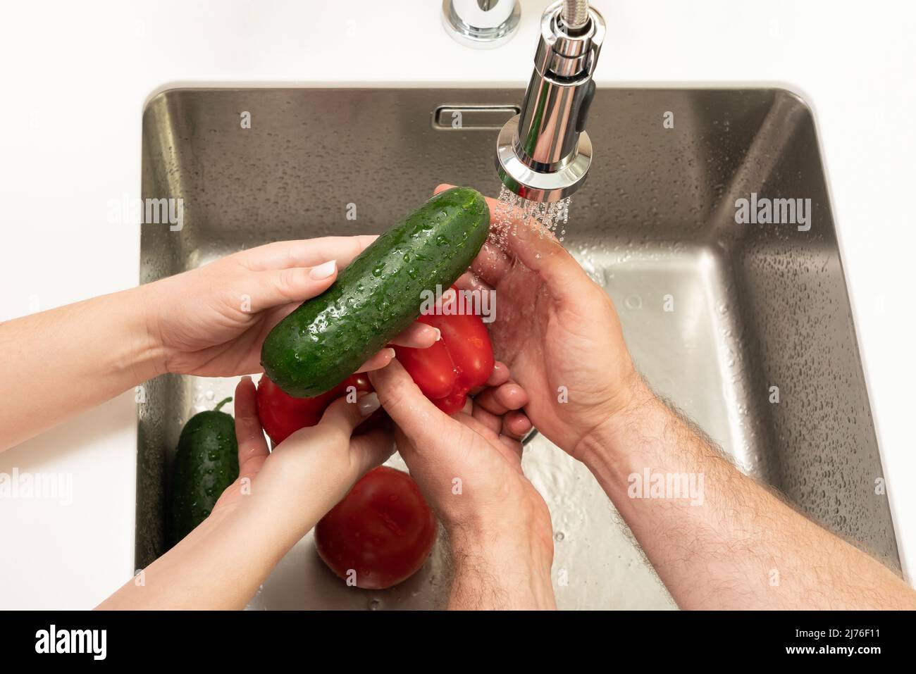 cucumbers and tomatoes are washed under running water in the sink Stock