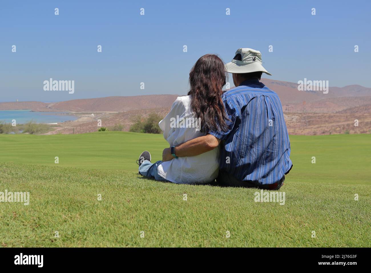 A loving couple sitting in the grass, relaxing while looking at the landscape. Stock Photo