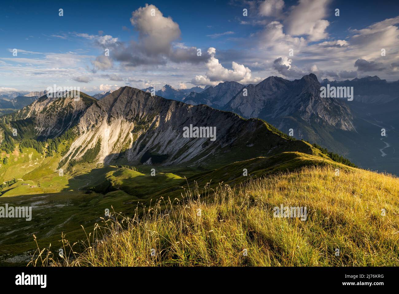 Late summer day with view from Schönalmspitze to Fleischbank, in the foreground golden grass and a mountain meadow, while the ridge leads to the next peak and light clouds shade parts of the picture. Stock Photo