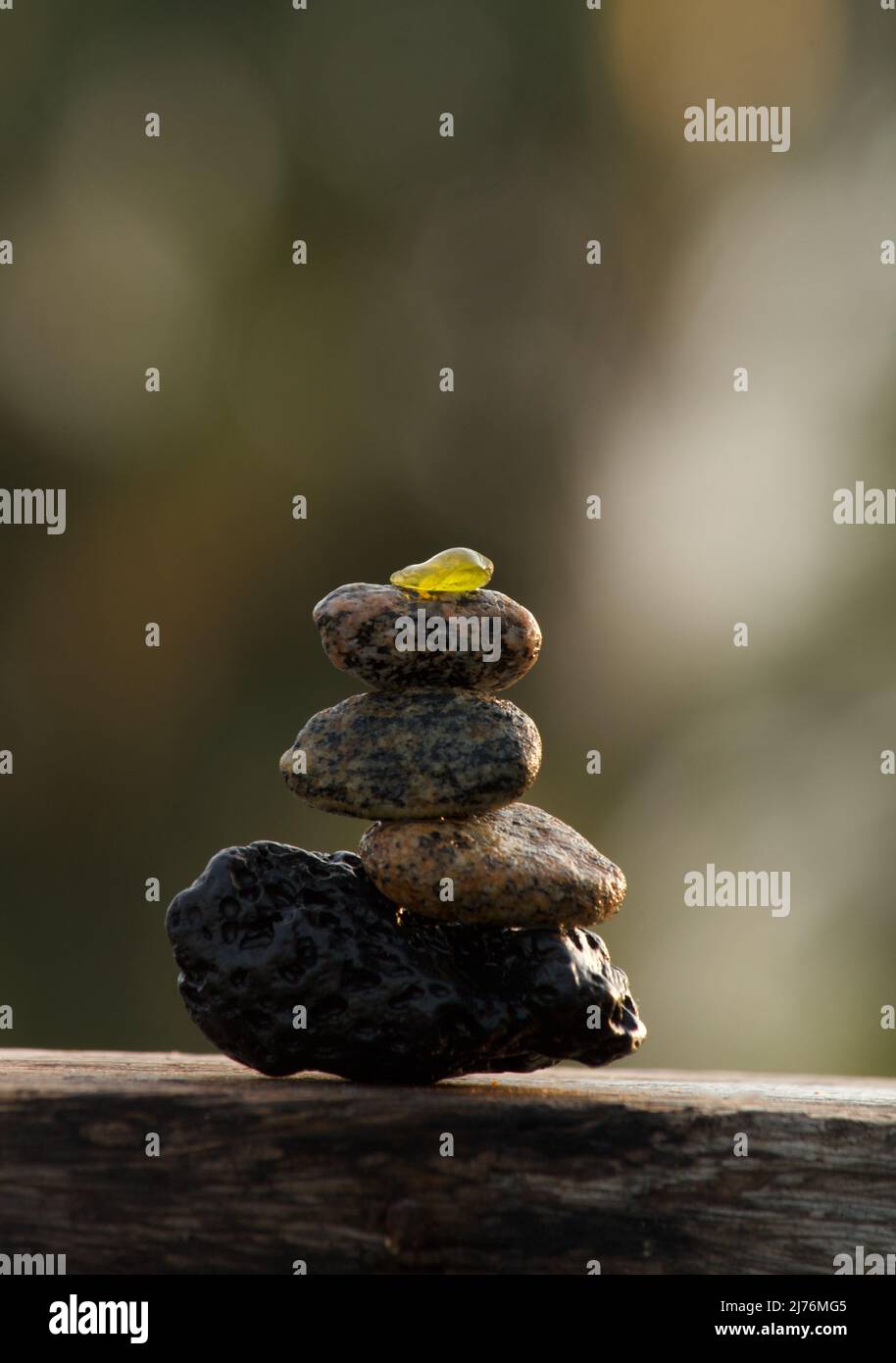 Different types of stone pebbles and tiny sea glass balance on a lava stone Stock Photo