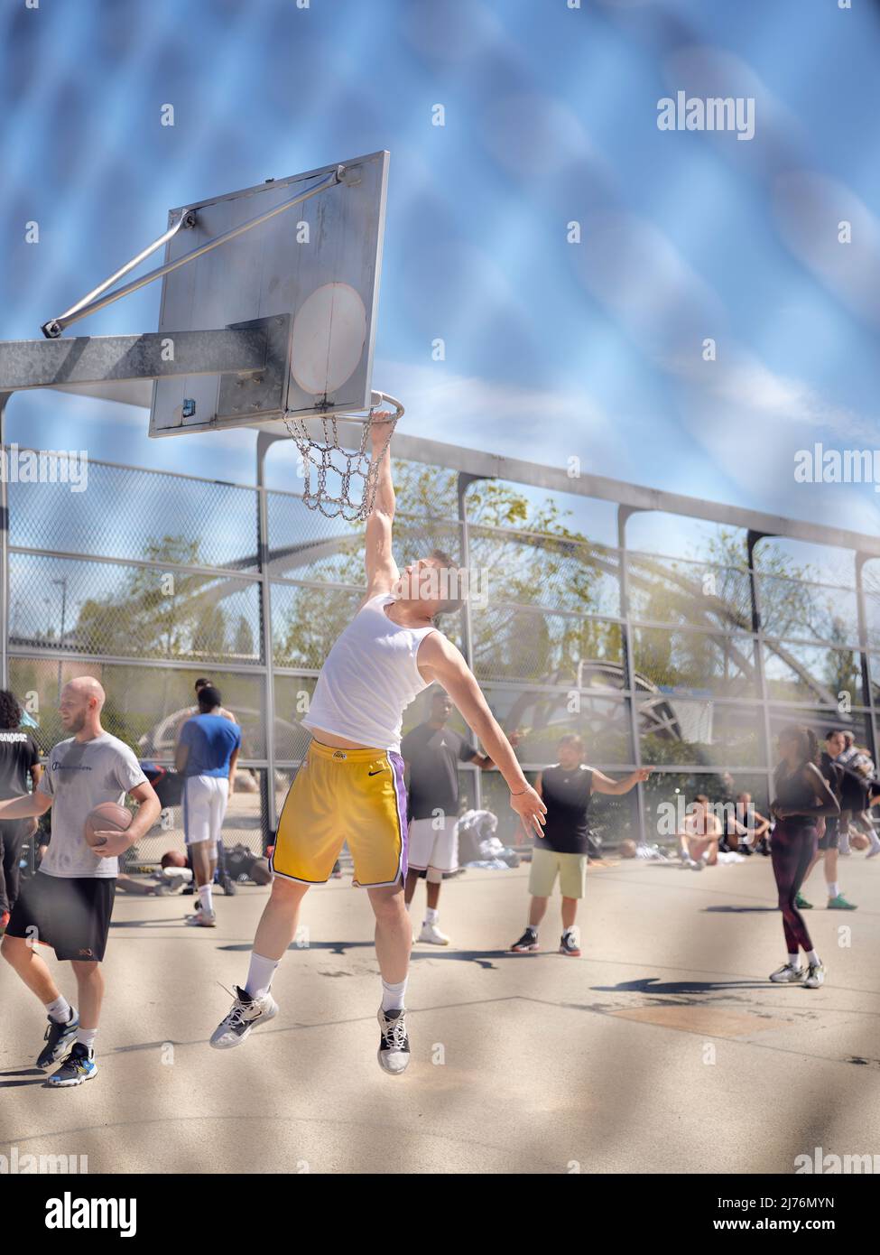 A young man has jumped to the basketball hoop and is holding on to it, in the harbor park in Frankfurt Stock Photo