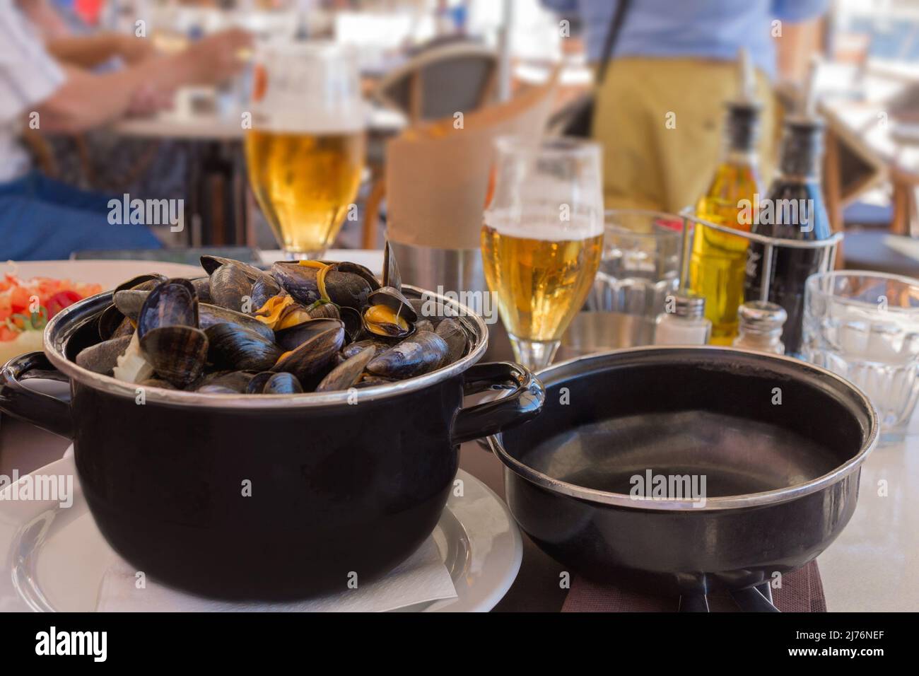 Cooked mussels in garlic sauce in a black saucepan on a table in a fish restaurant. Delicious lunch with seafood and beer. Gastronomic travel. Close-u Stock Photo