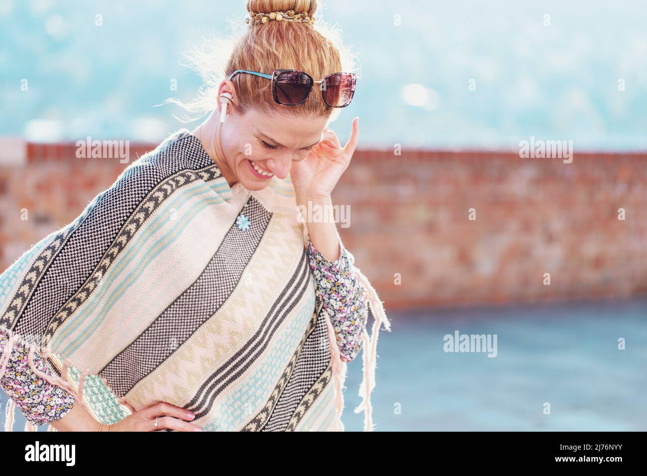 Young trendy hipster woman in poncho listening music by earphones outdoors Stock Photo