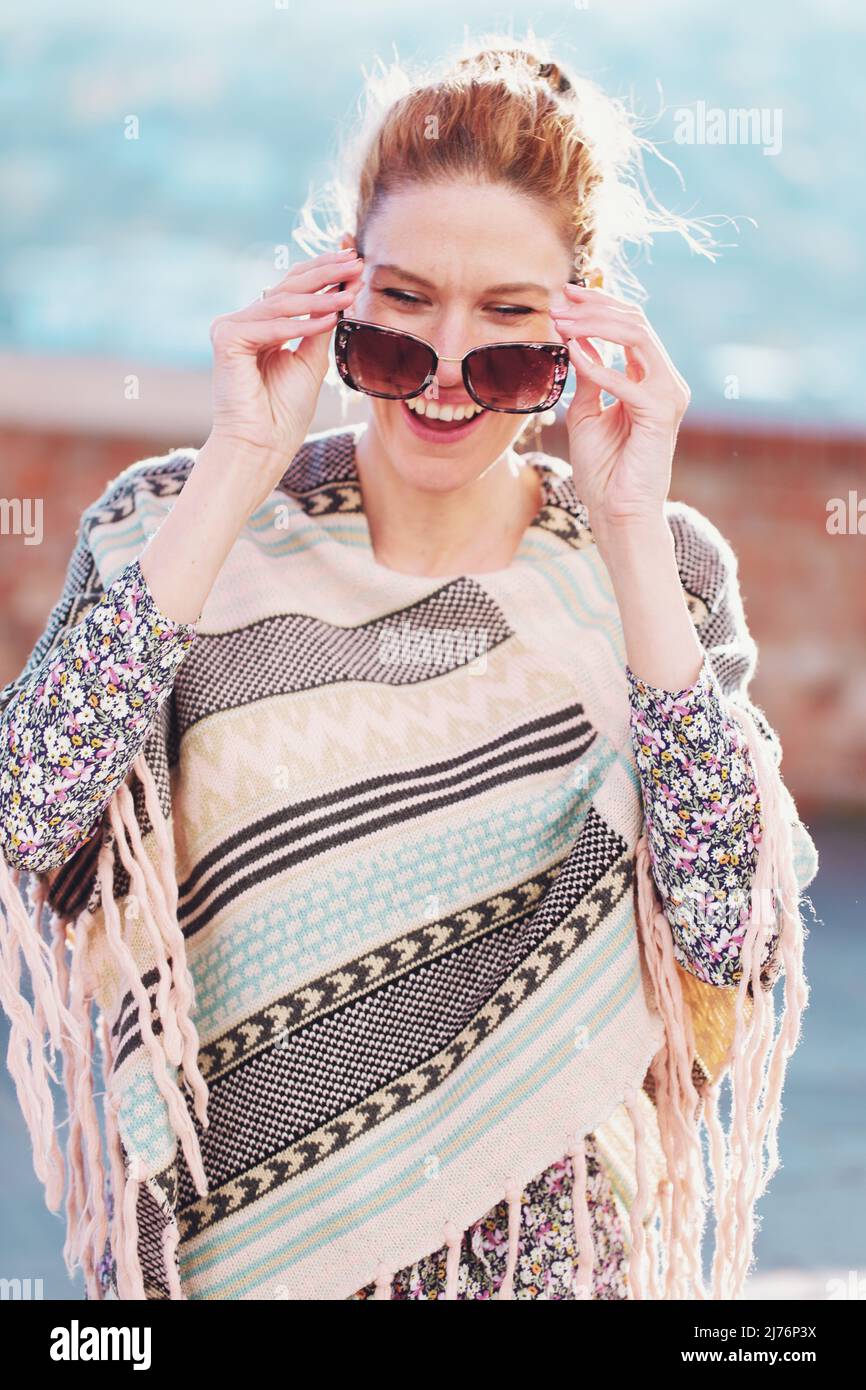 Happy young redhead woman in poncho laughing outdoors, life balance Stock Photo