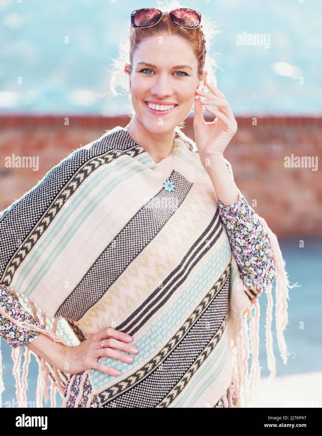 Young balanced woman in poncho toothy smile while calling by hands free device Stock Photo