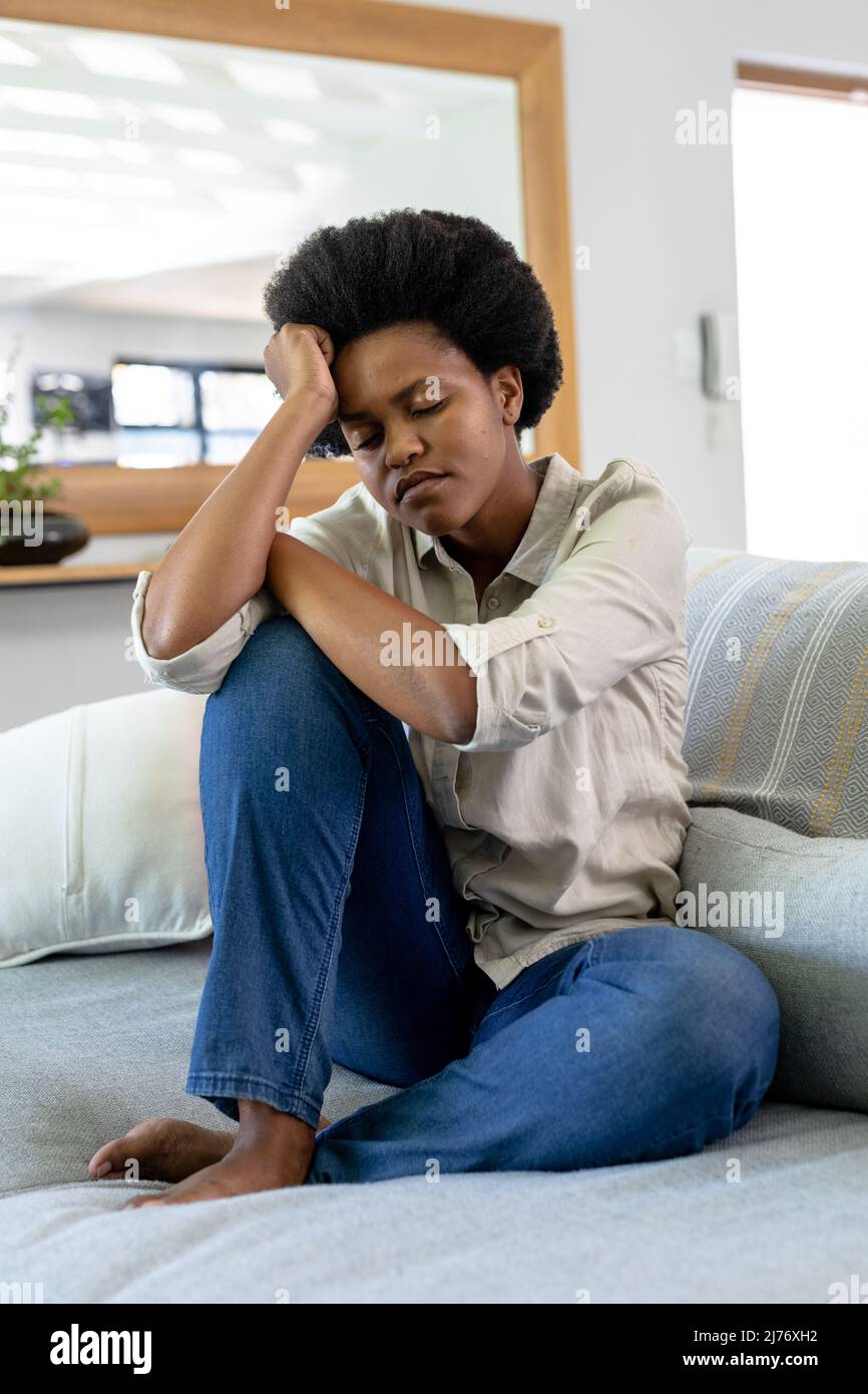 Sad mid adult african american woman sitting with eyes closed on sofa ...