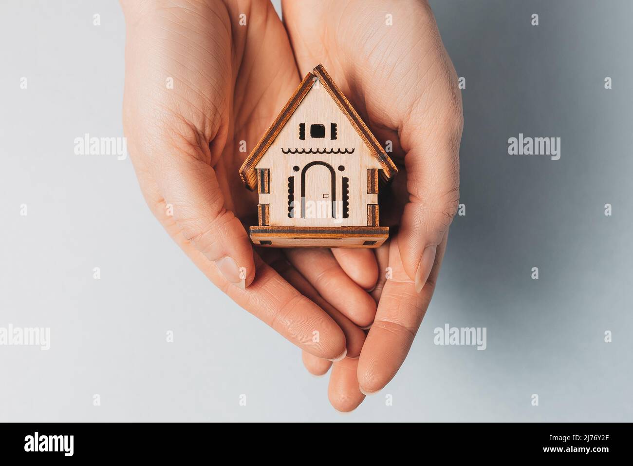 Woman holding a wooden house with her hands with the sun on a light ...